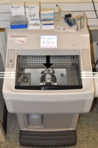 Figure 1: Cryostat currently in use at Angell. The microtome (denoted by the wide black arrow) is housed within the freezing chamber, which can be seen/accessed through the large sliding glass window at the center (delineated by thin white arrows). The chamber is kept at a temperature of about -20⁰C until the time of sectioning, at which time it is dropped to -40⁰C